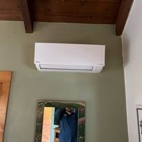 White air conditioning unit mounted on a green wall, above a mirror reflecting a person.