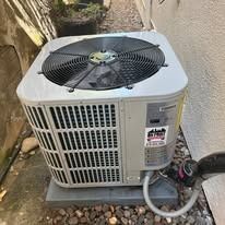 Outdoor air conditioning unit. Gray metal box with fan, set on concrete, in alley.