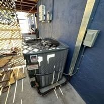 Air conditioning unit outside a building with a blue wall and metal pipes.