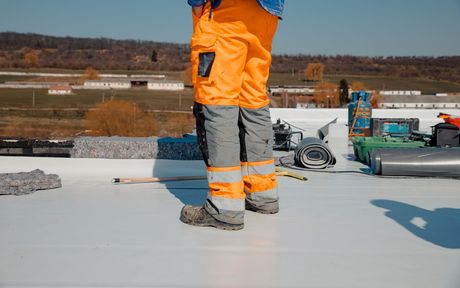 legs of a worker wearing an orange work pants with the tools lying around