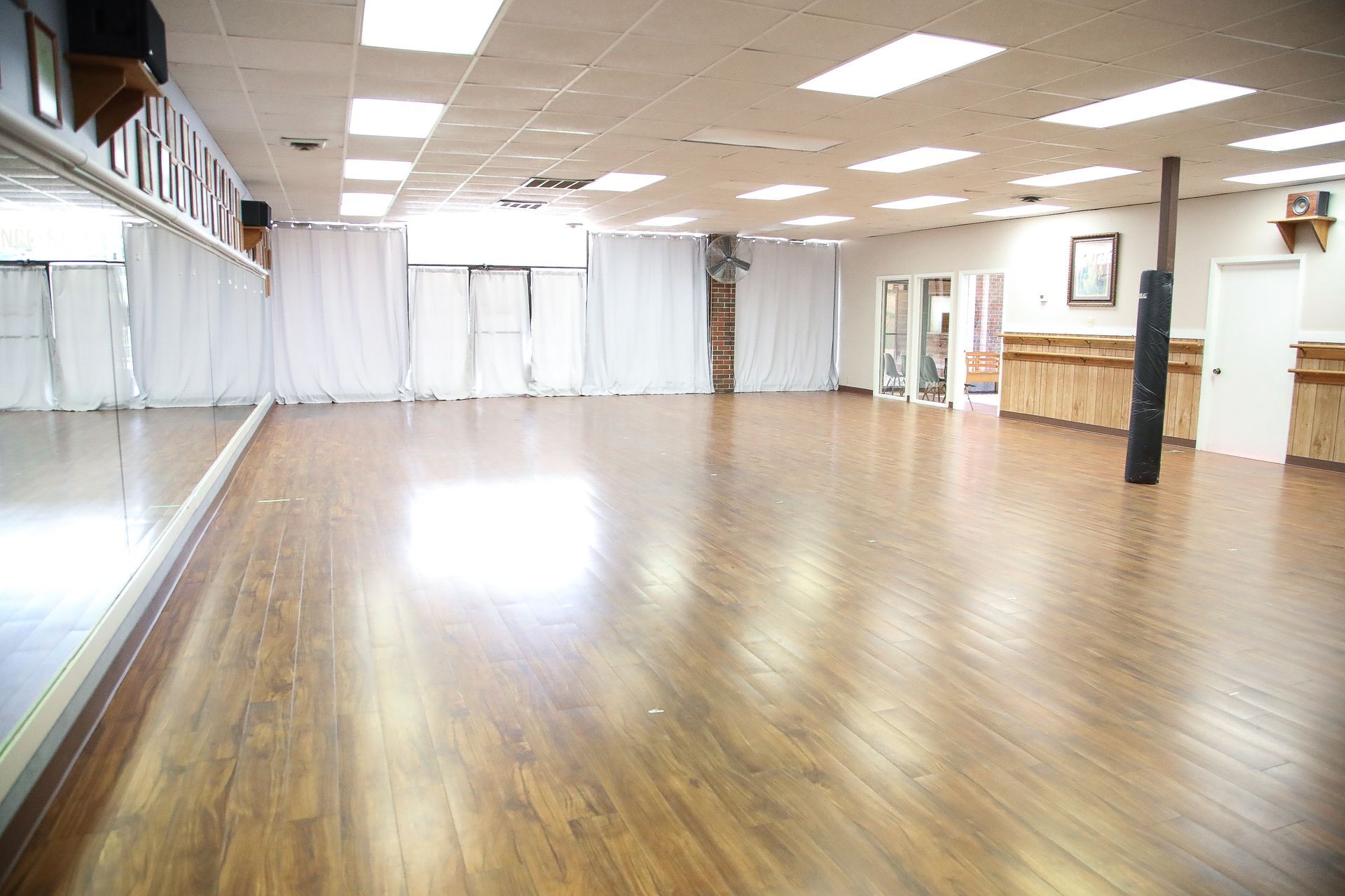 Dance studio with wood floor, large mirrors, white curtains, and bright lighting.