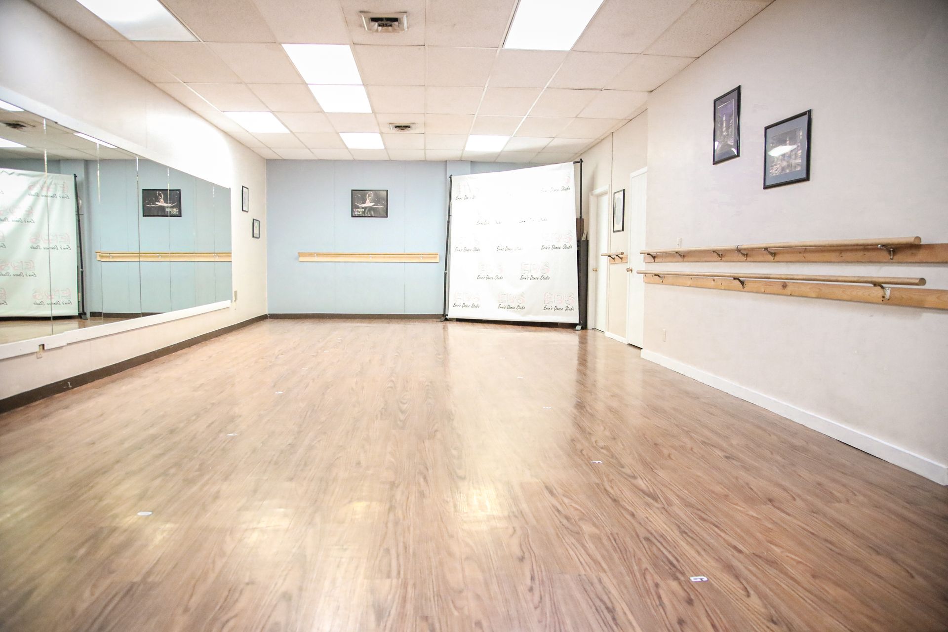 Empty dance studio with wood floor, mirrors, and barres.