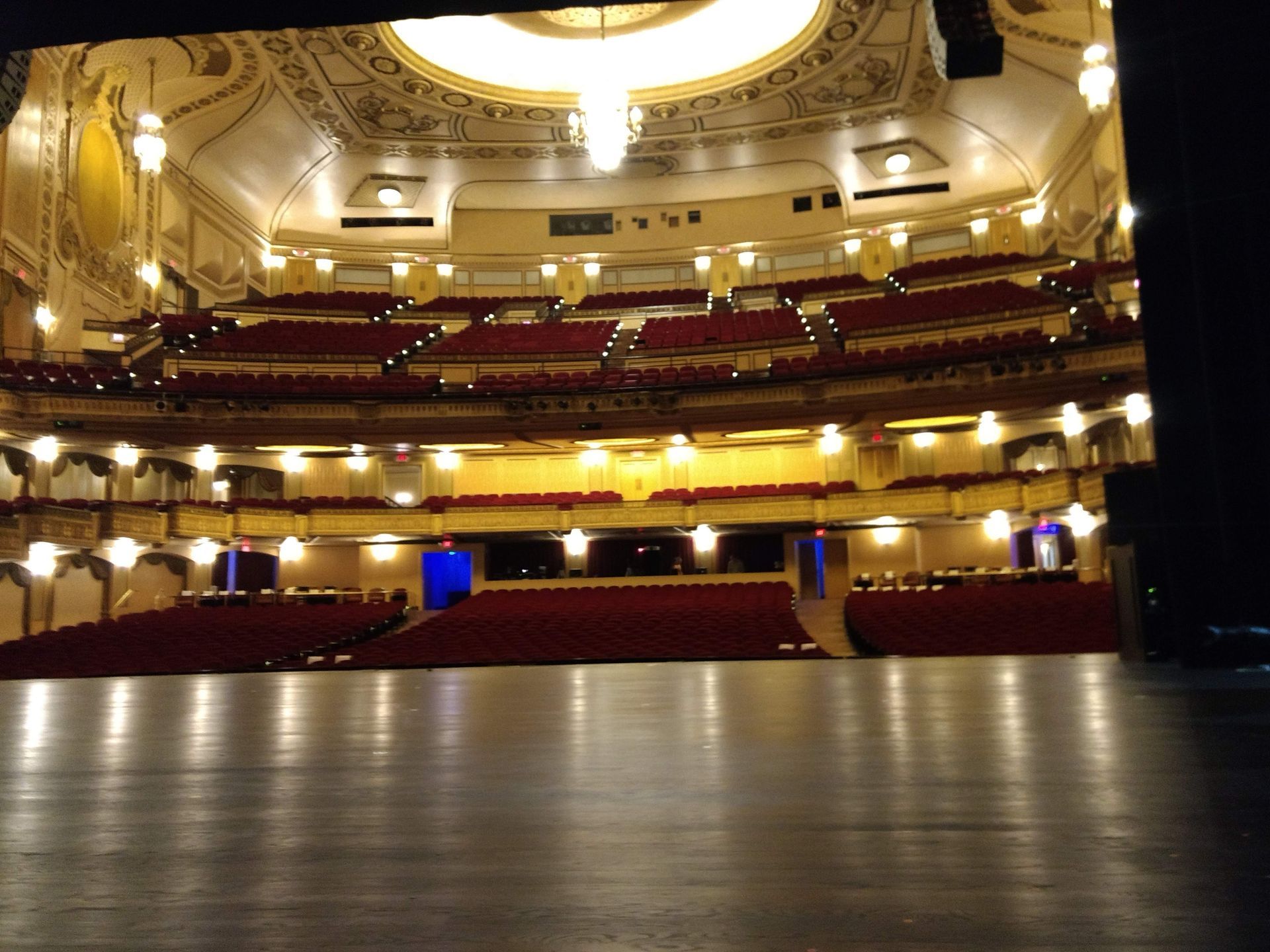 View from a theater stage looking out at empty red seats and ornate gold ceiling.