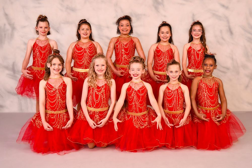 Group of young girls in matching red dance costumes posing in a studio. They are smiling.
