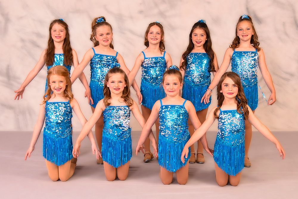 Group of young girls in blue sequined dance costumes, posing with arms outstretched.