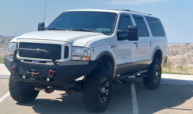 White Ford Excursion SUV with off-road modifications, parked outside on a sunny day.