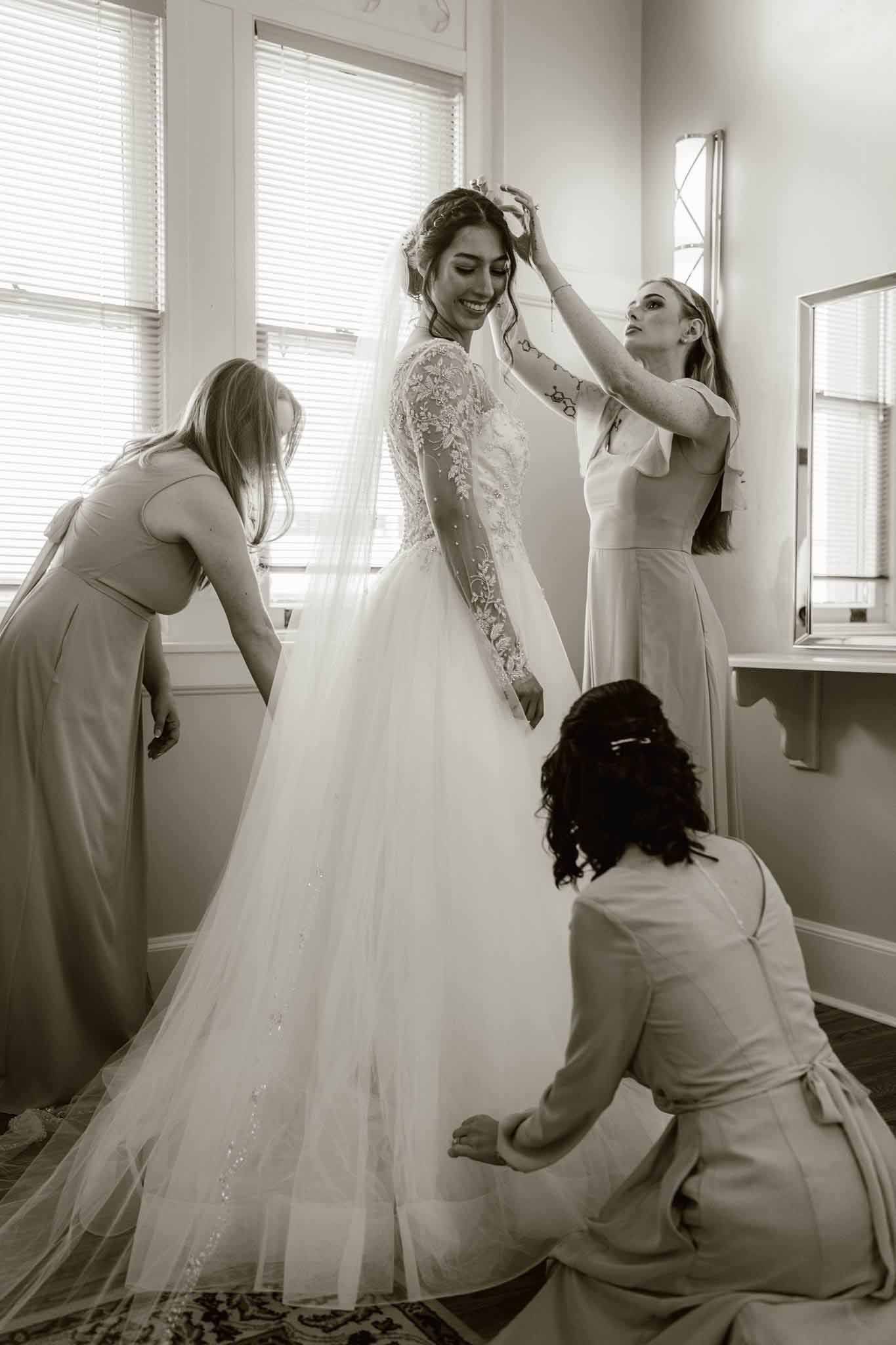 A black and white photo of a bride and her bridesmaids getting ready for her wedding.