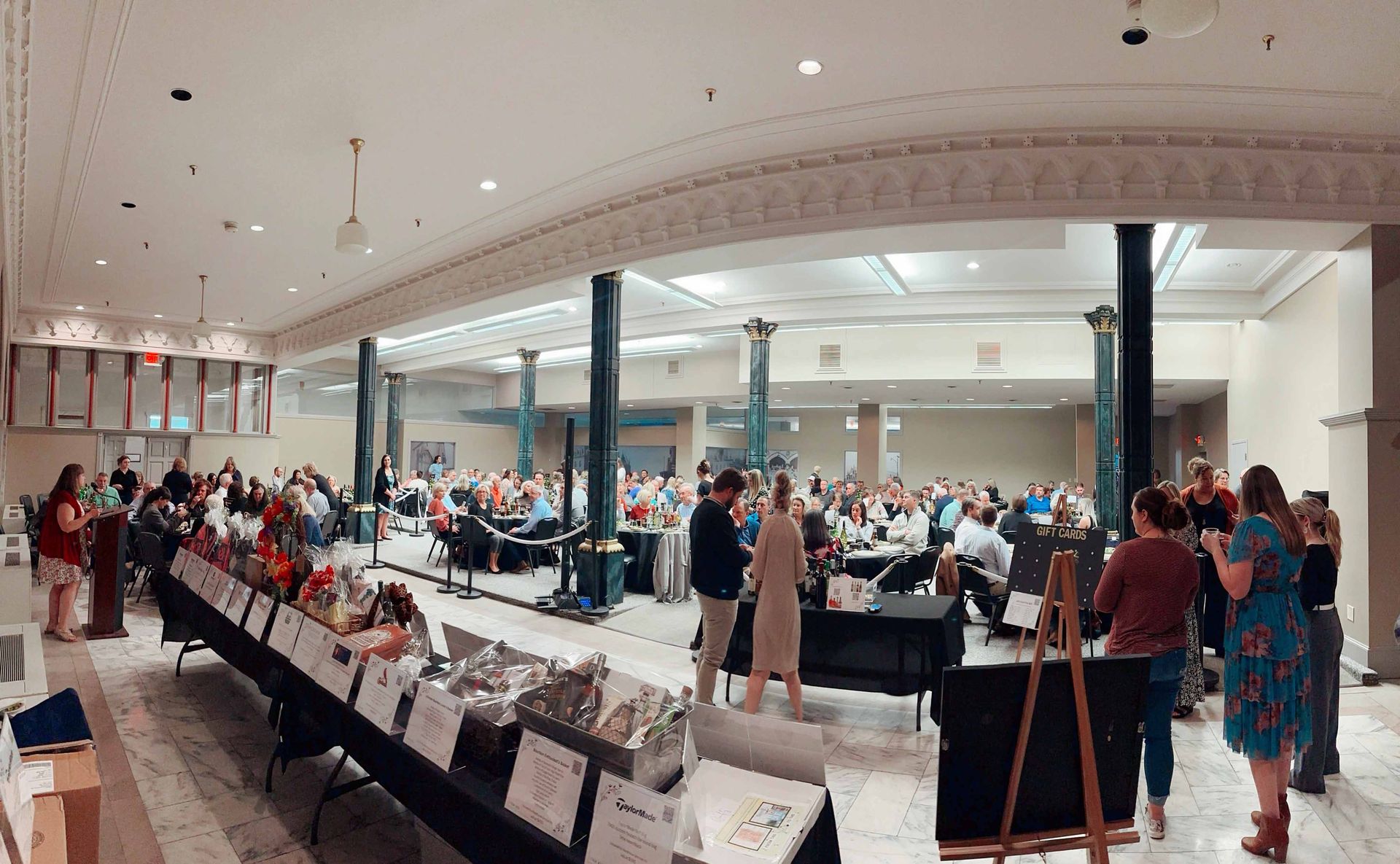 A large room filled with people standing around tables.