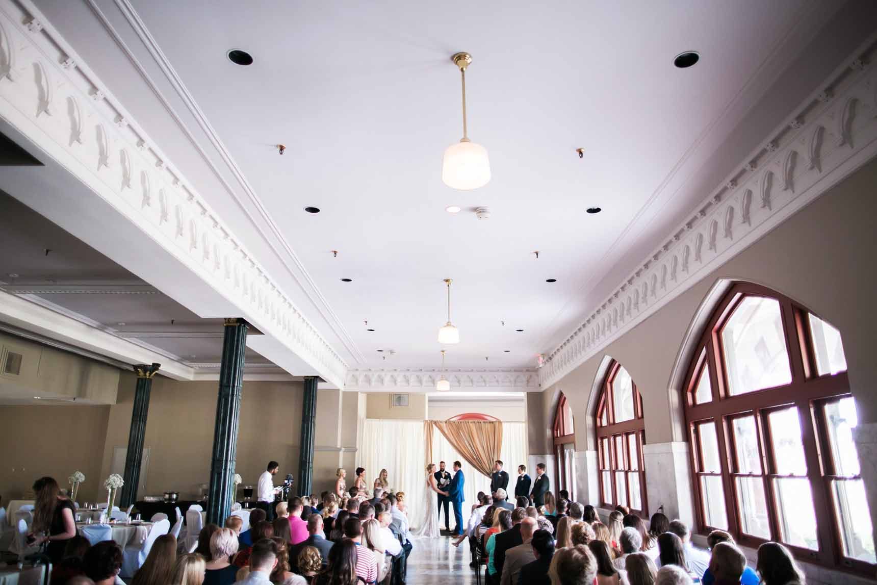 A group of people are sitting in a large room watching a wedding ceremony.