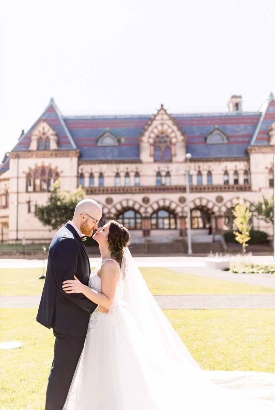 A bride and groom are kissing in front of a large building.