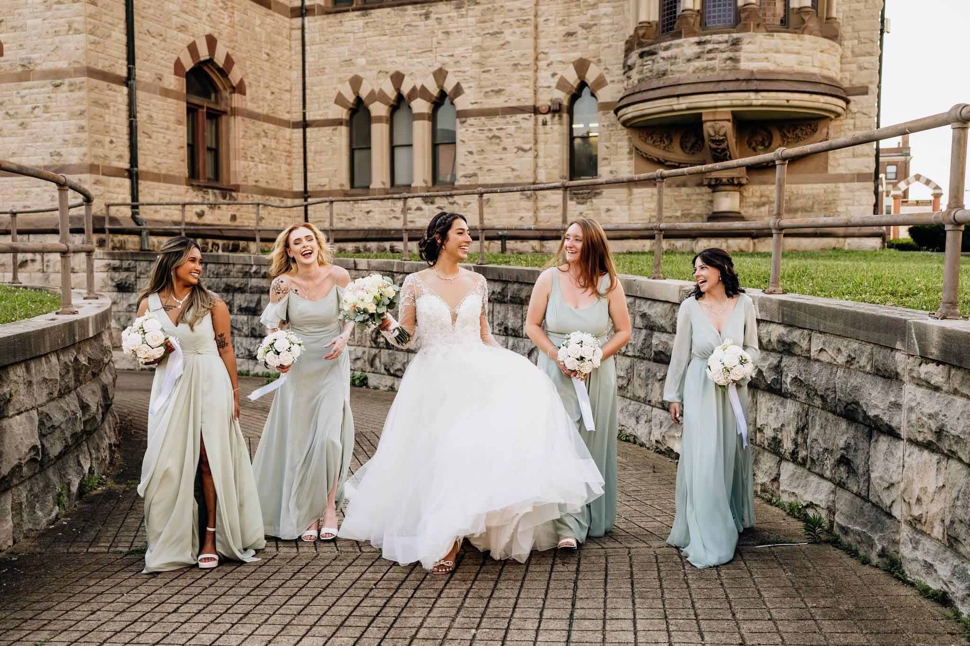 A bride and her bridesmaids are walking down a sidewalk in front of a building.