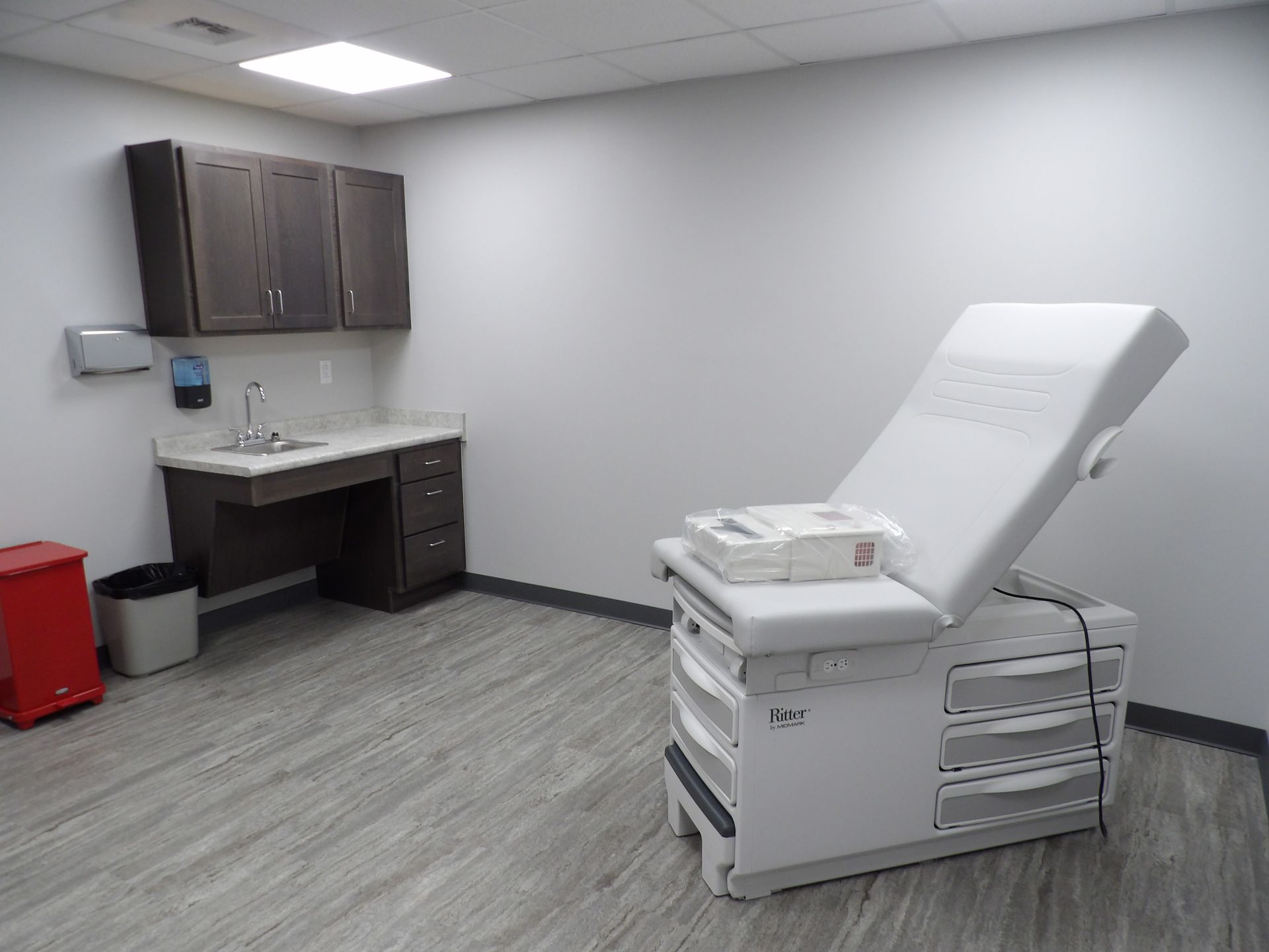 A doctor 's office with a white examination table and a sink.