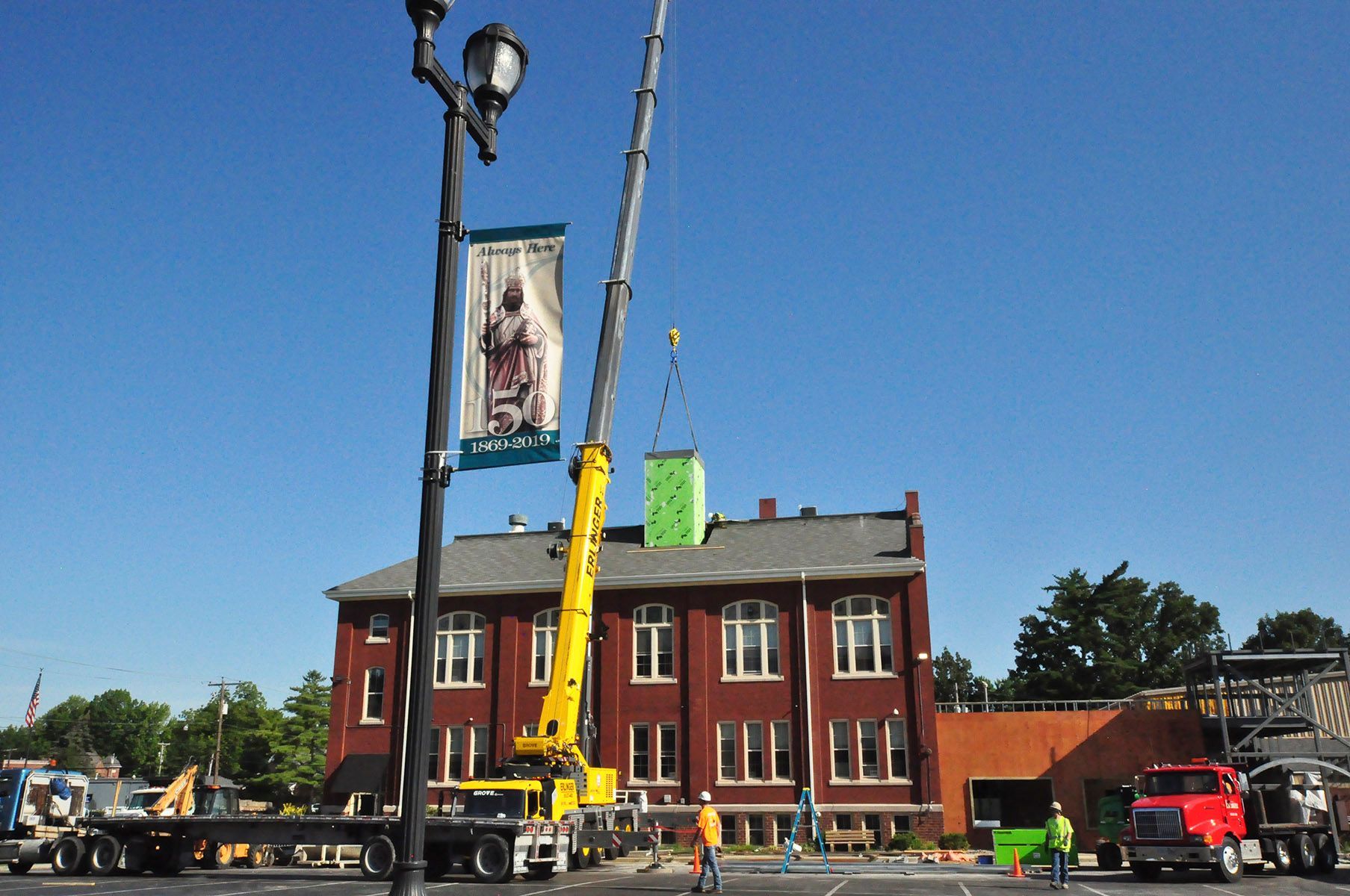 A yellow crane is lifting a box in front of a brick building