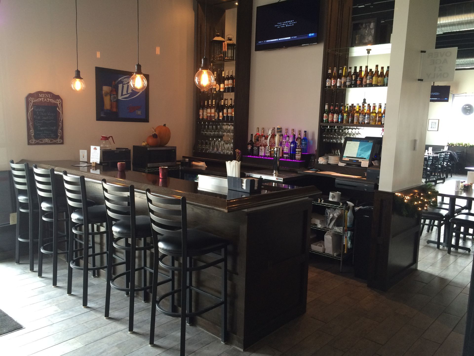 A bar in a restaurant with a miller lite logo on the wall