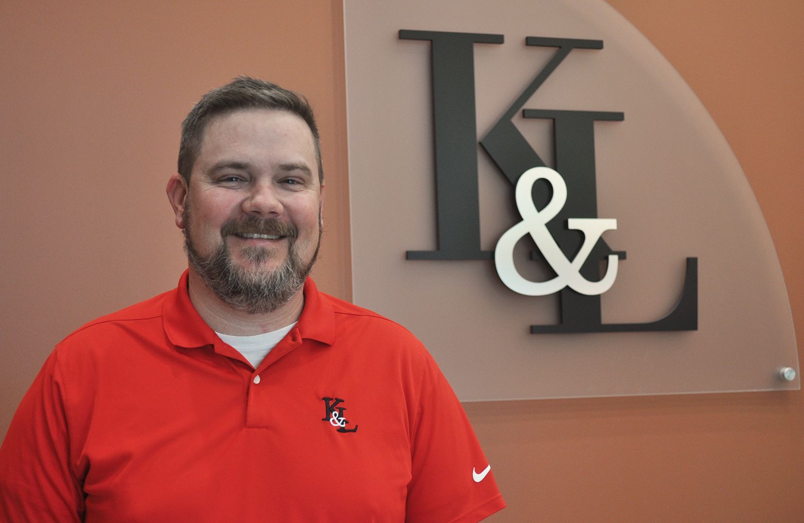 A man in a red shirt is standing in front of a sign that says k & l.