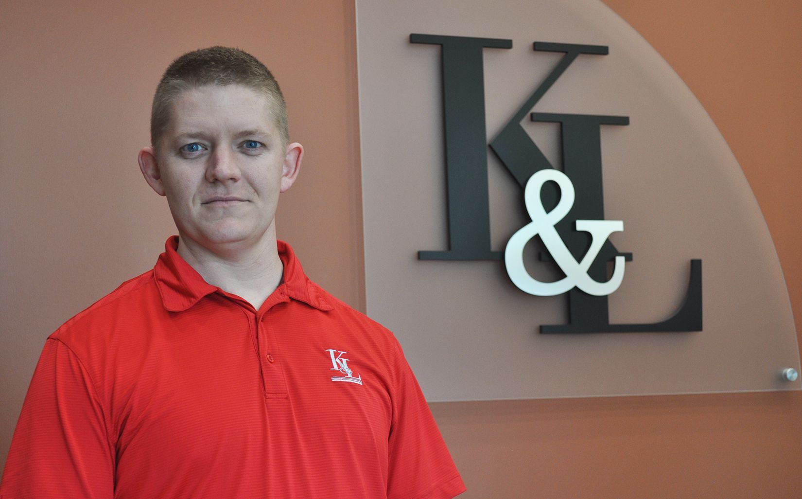 A man in a red shirt is standing in front of a sign that says k & l