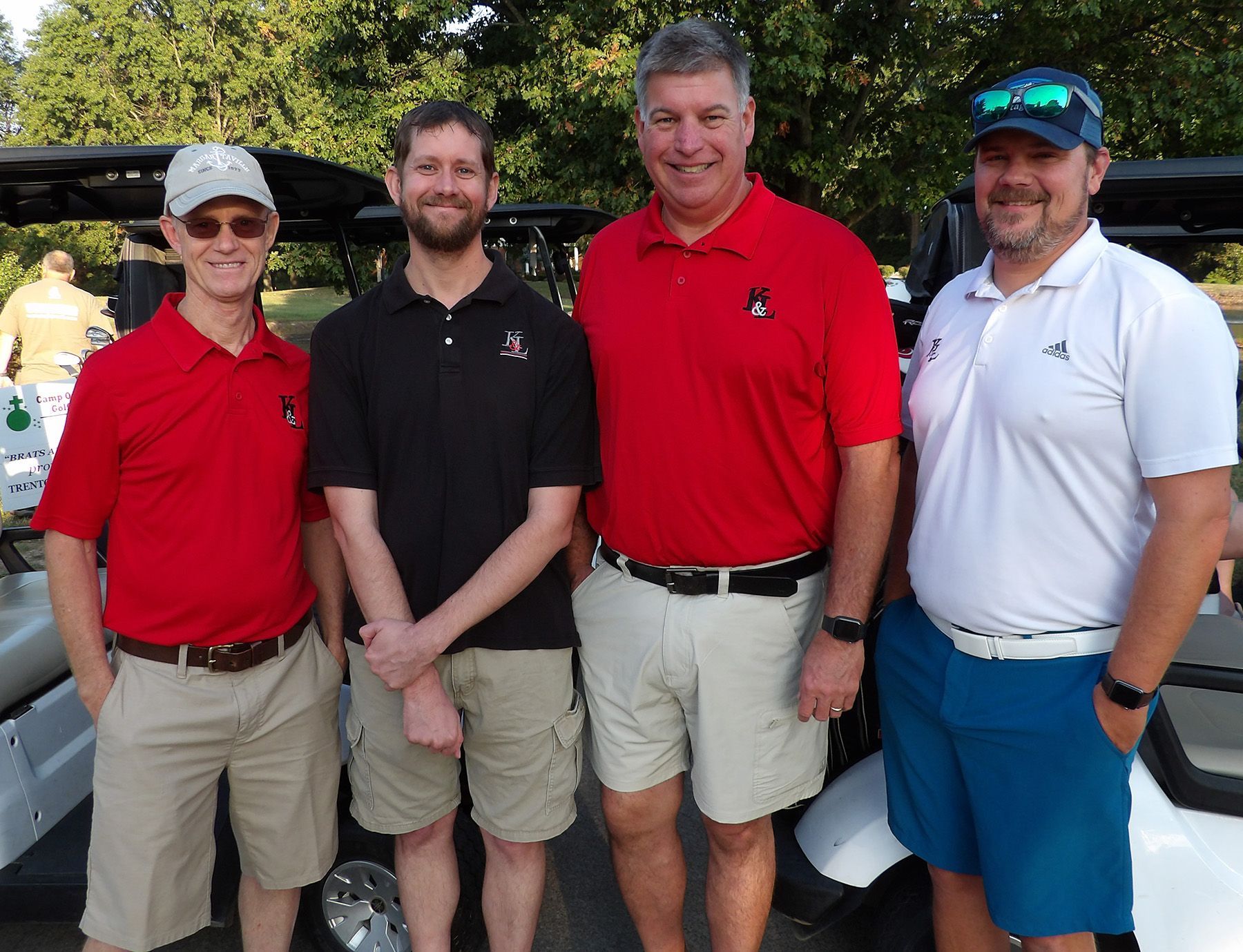 Four men are posing for a picture in front of a golf cart