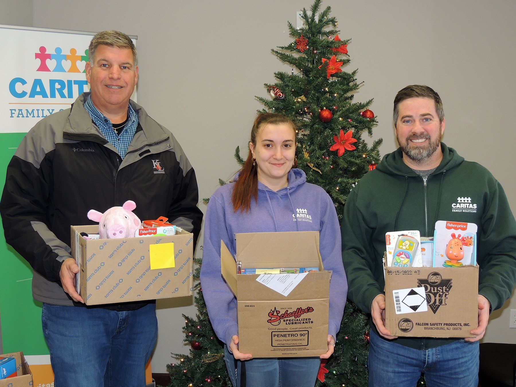 Three people are holding boxes in front of a christmas tree.