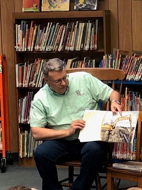 A man in a green shirt is reading a book in a library