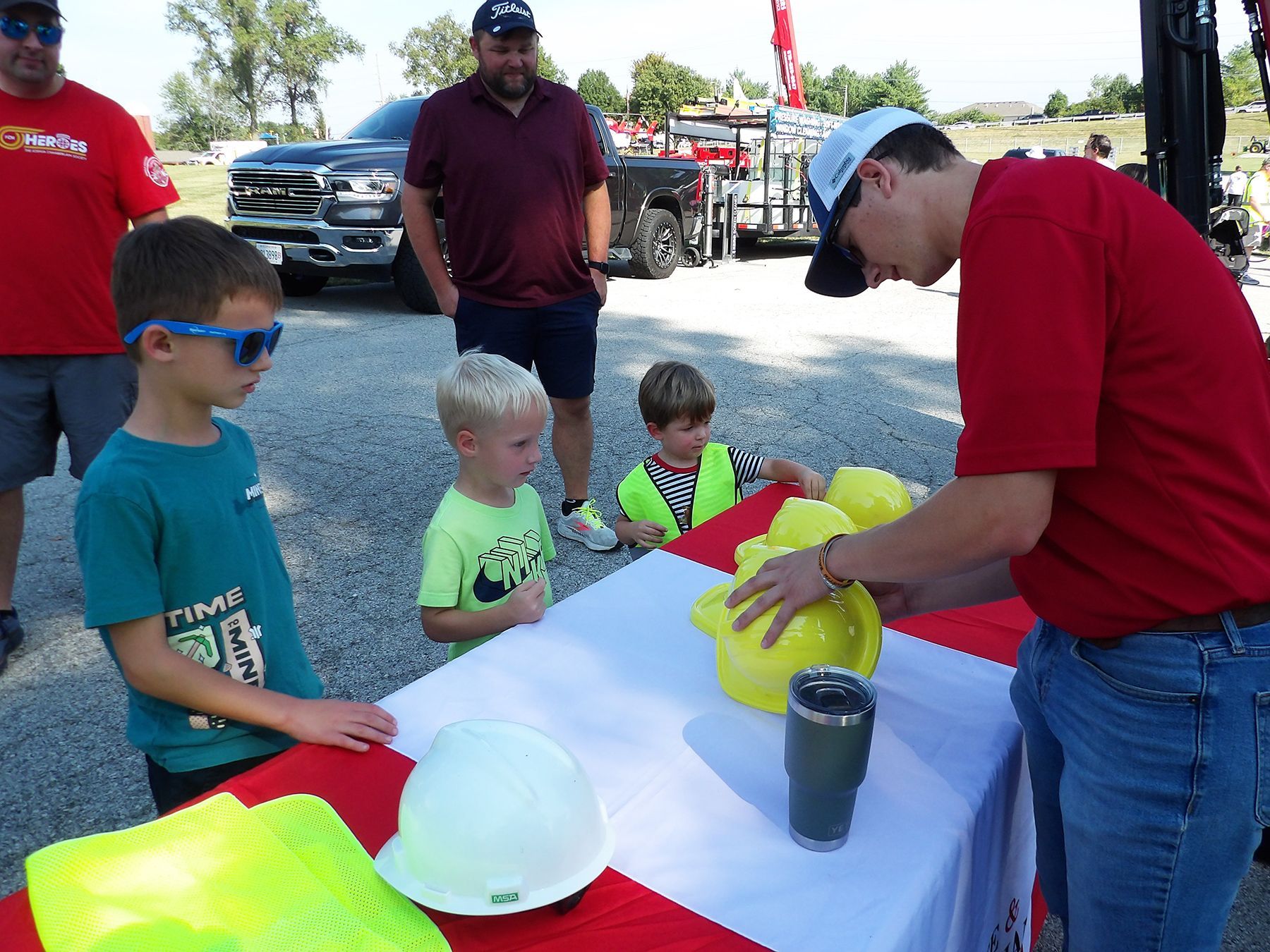 A man in a red shirt is putting a yellow hard hat on a table.