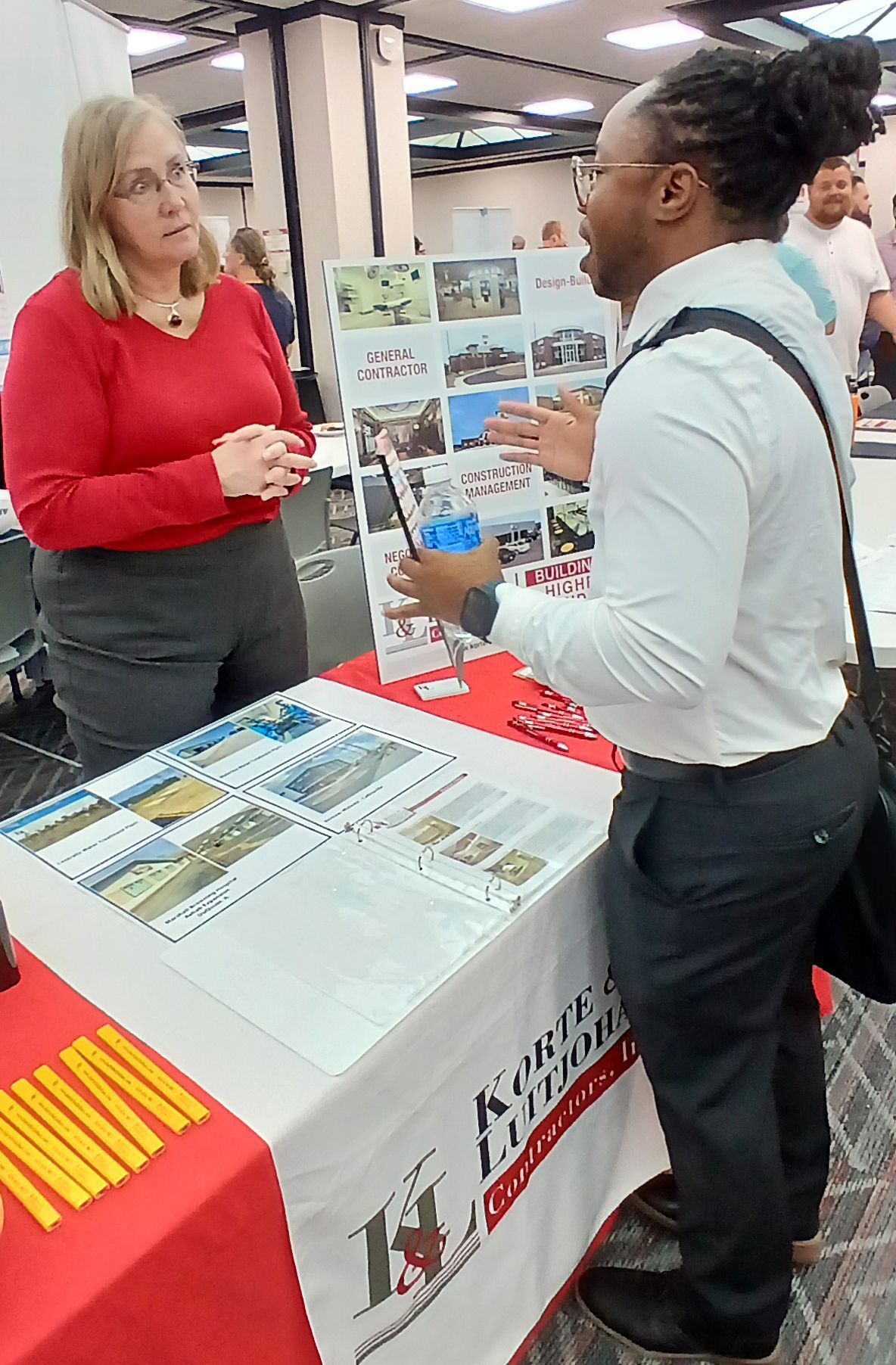 A man and a woman are standing at a table talking to each other.