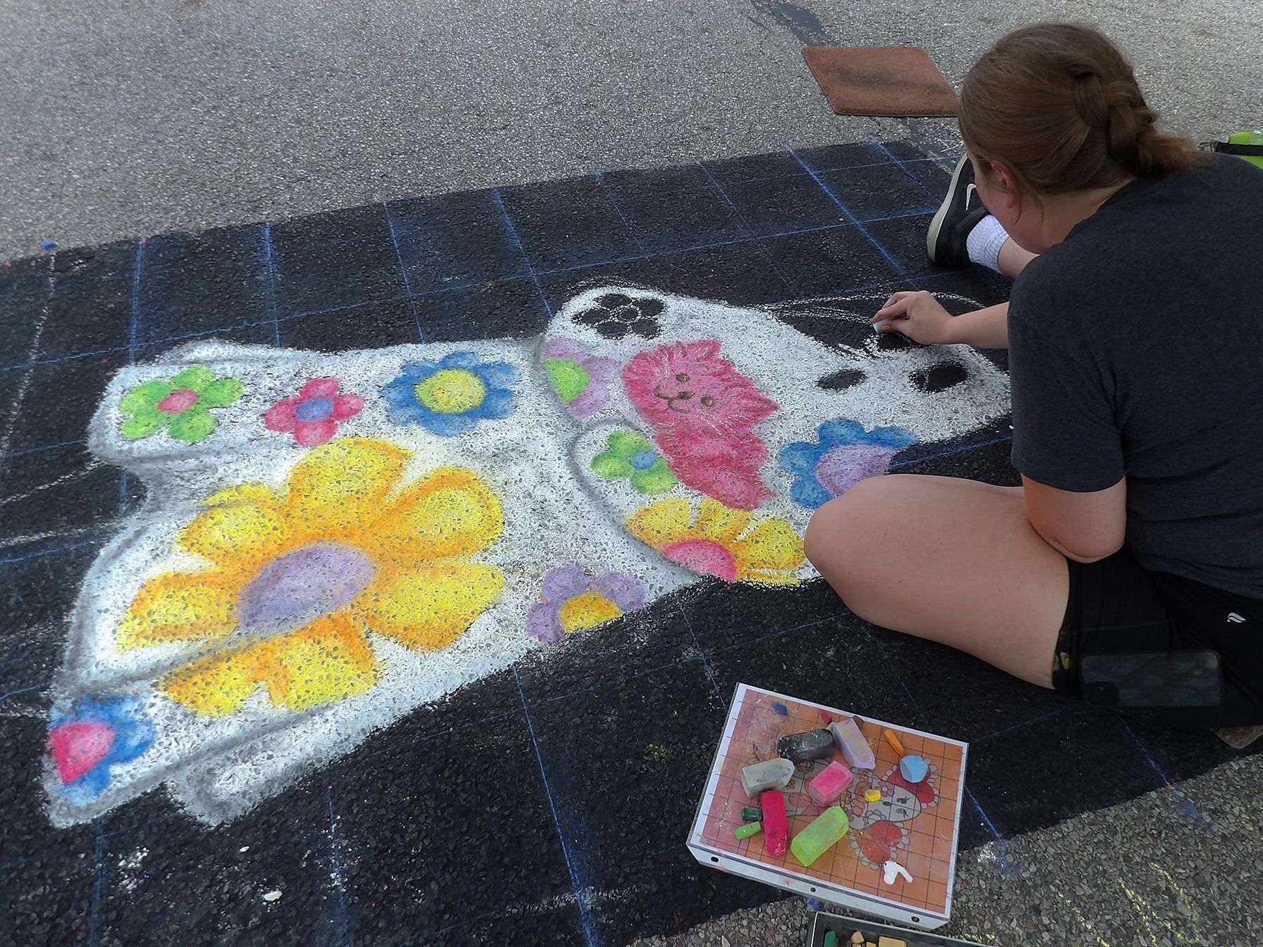 A woman is sitting on the ground painting a dog with flowers