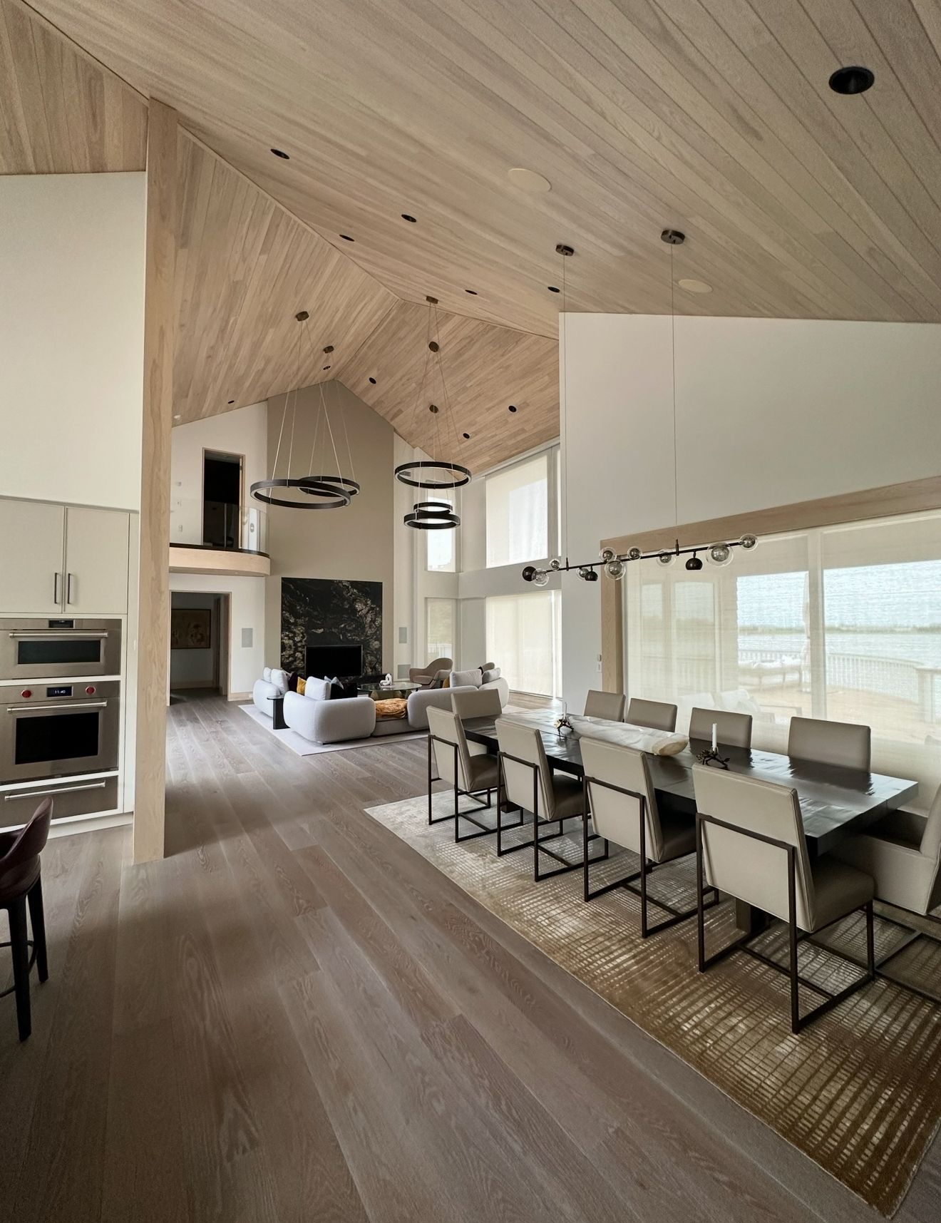 Spacious, modern dining and living area with high vaulted, wood-paneled ceilings. Long dining table with chairs, and a living area with a fireplace.