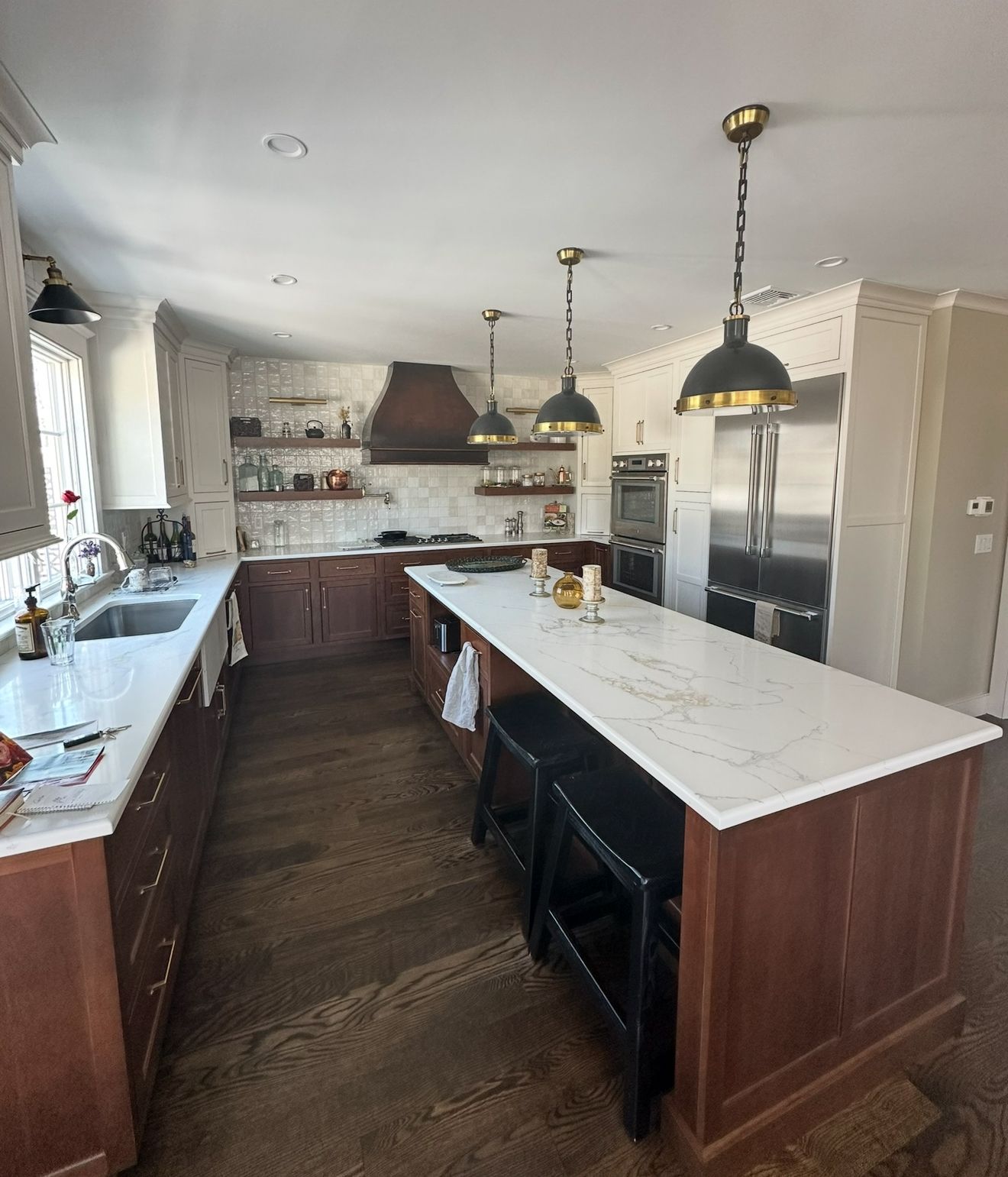 A modern kitchen with a large island, dark wood cabinets, white countertops, and three pendant lights.