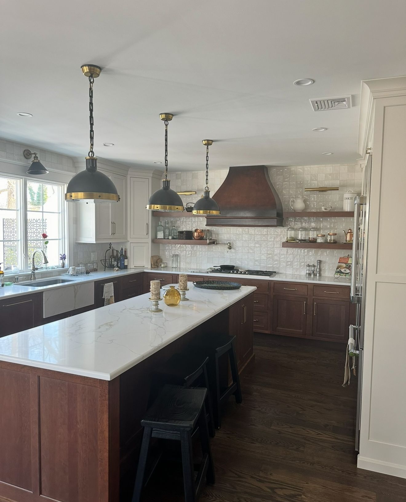 A kitchen with a large island, dark wood cabinets, white countertops, and pendant lights. A copper range hood is centered above the stove.