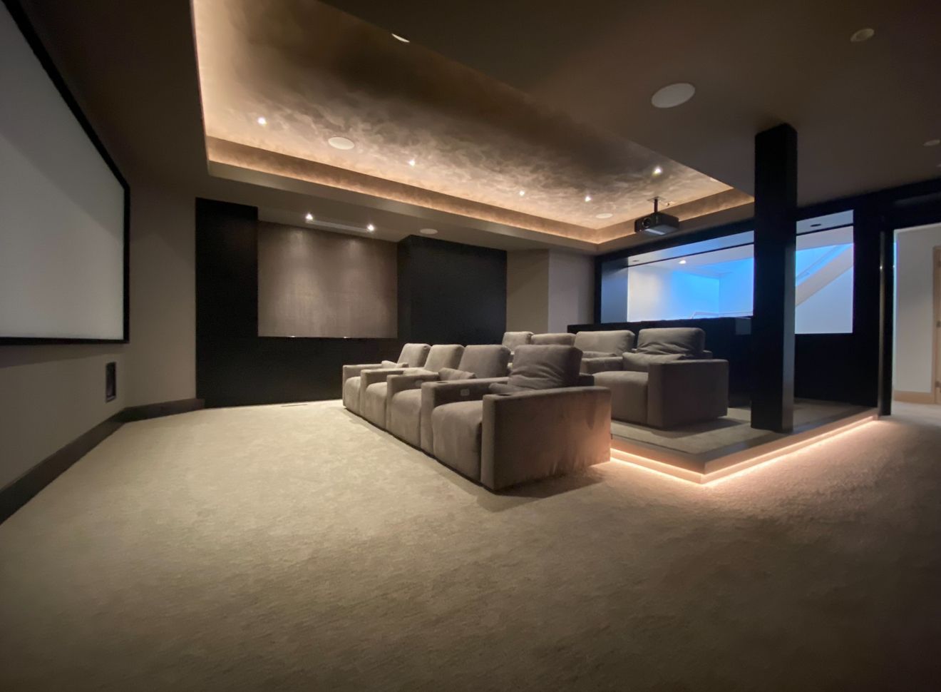 A luxurious home theater with tiered seating and a large screen. Soft lighting illuminates the plush couches and textured ceiling.
