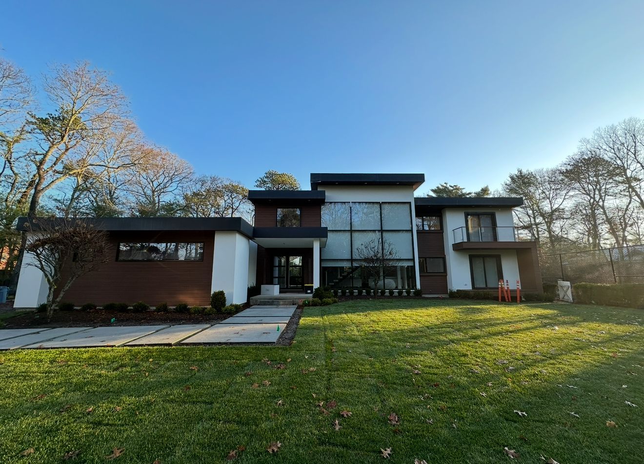 Modern two-story house with white and brown exterior, large glass windows, and a green lawn under a clear blue sky.