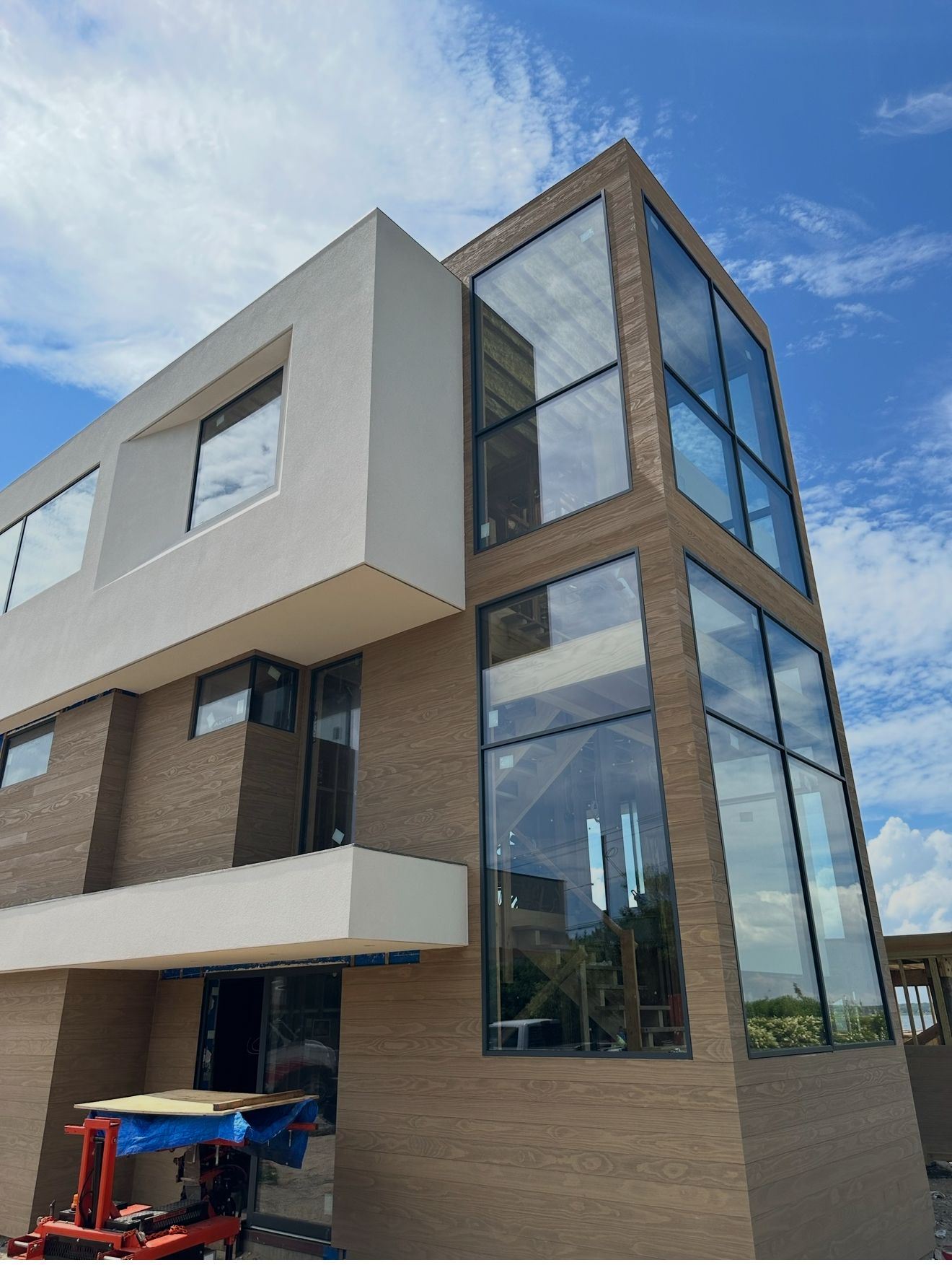 Modern building with tan brick facade and large glass windows against a cloudy blue sky. A white overhang is on the upper left.