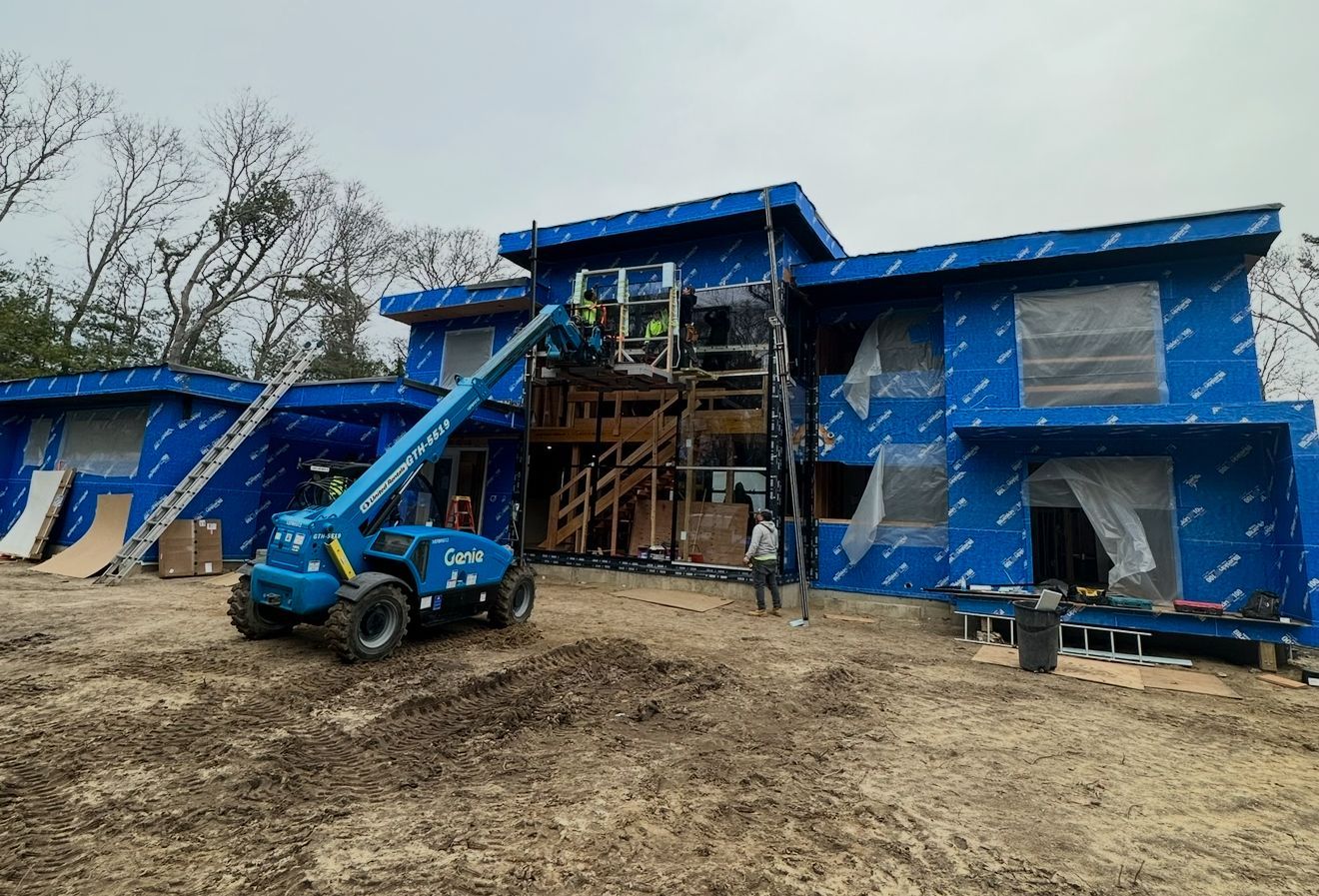 A blue lift raises workers to a building under construction. The building has blue siding and partially covered windows.