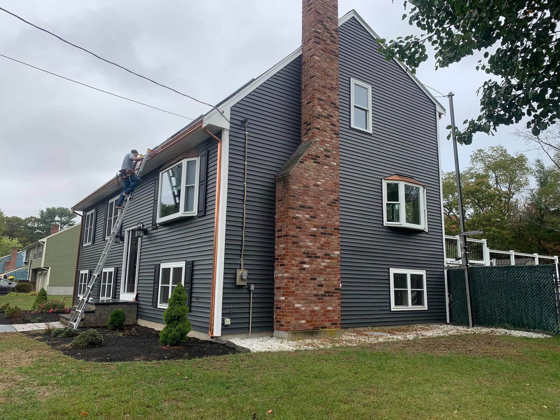 Gray shingle house with red brick chimney and white-trimmed windows on a grassy corner lot.