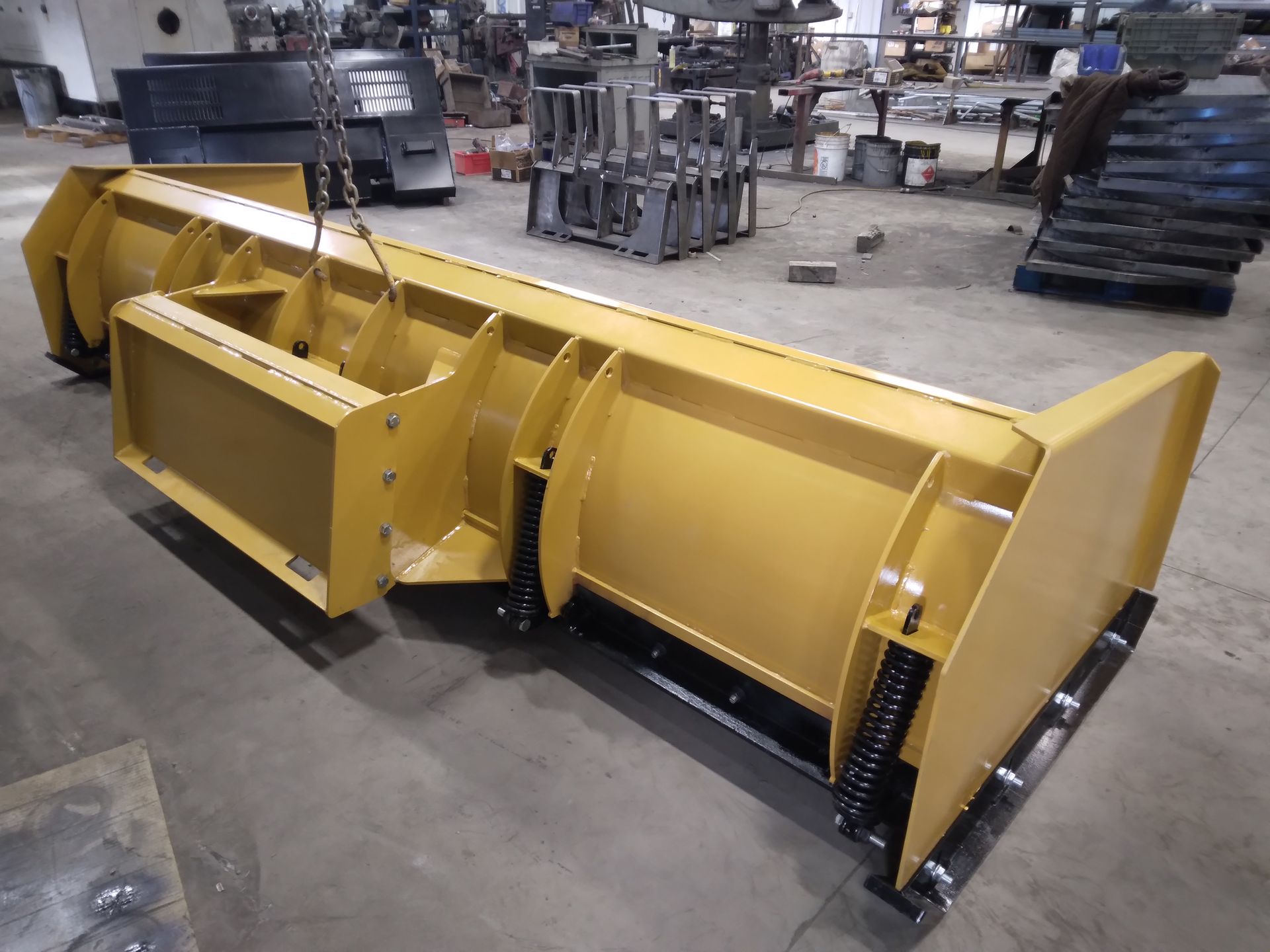 A yellow snow plow is sitting on the ground in a factory.