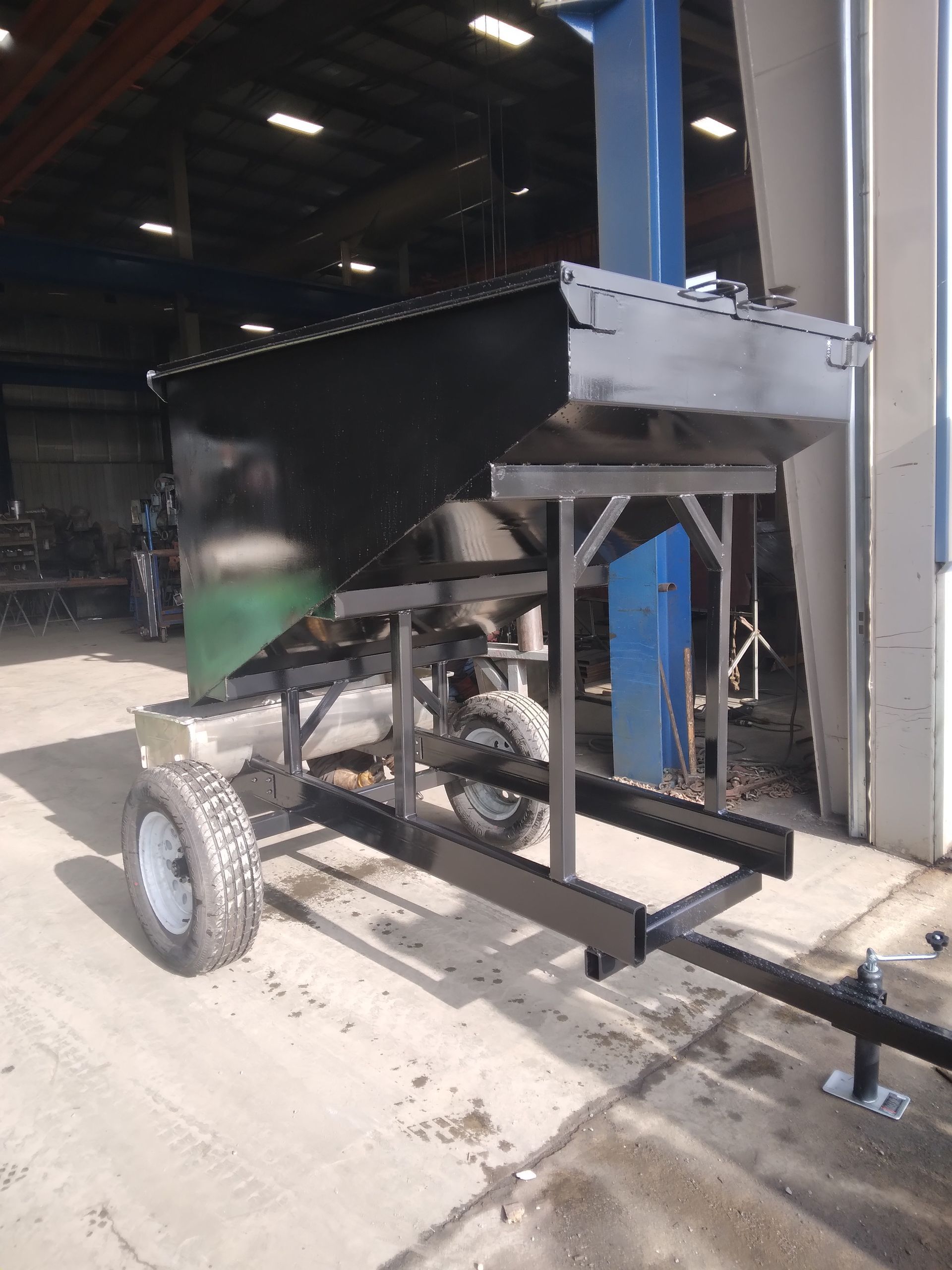 A black trailer with wheels is parked in front of a building.