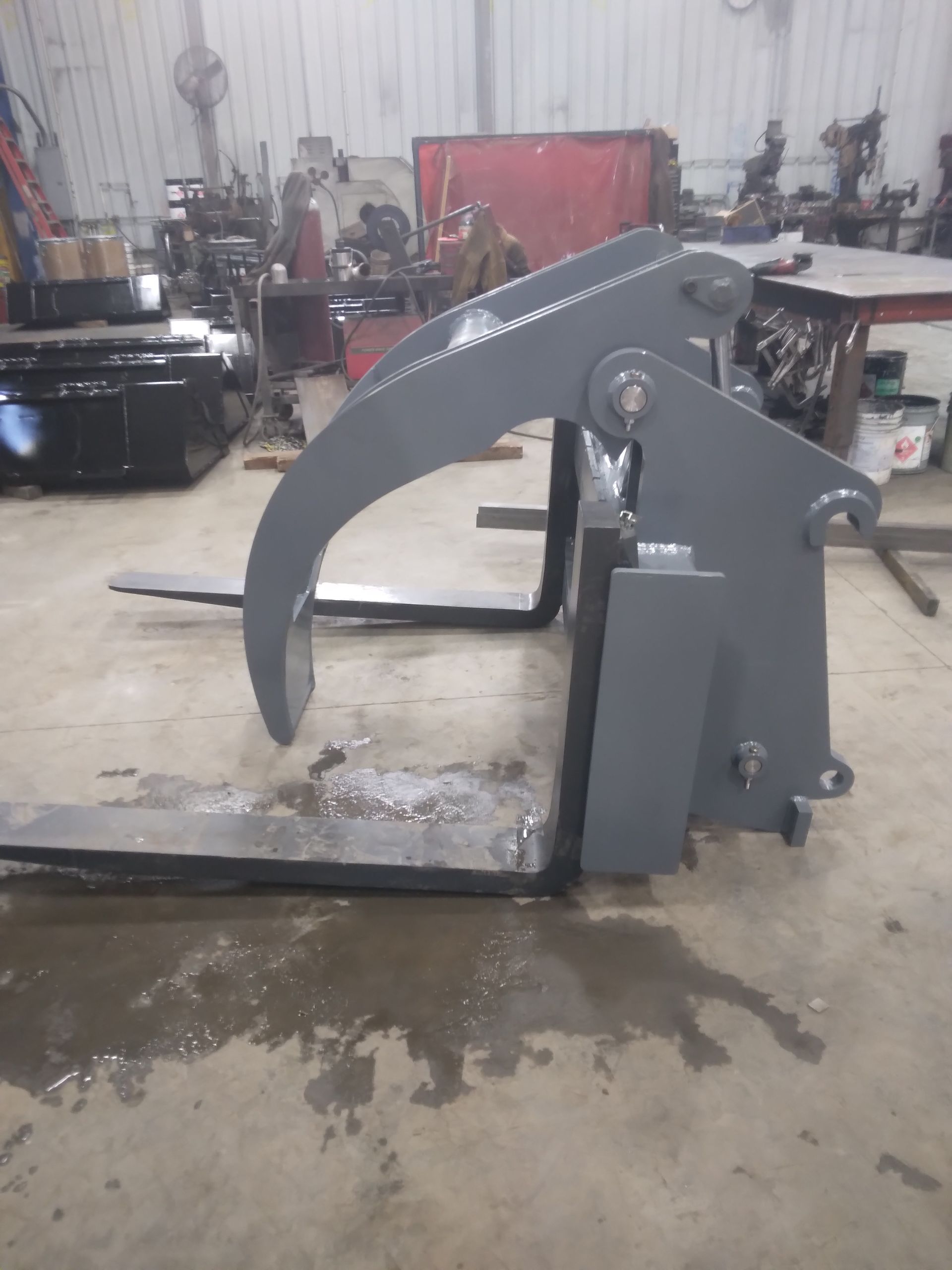 A forklift grapple is sitting on the ground in a garage.