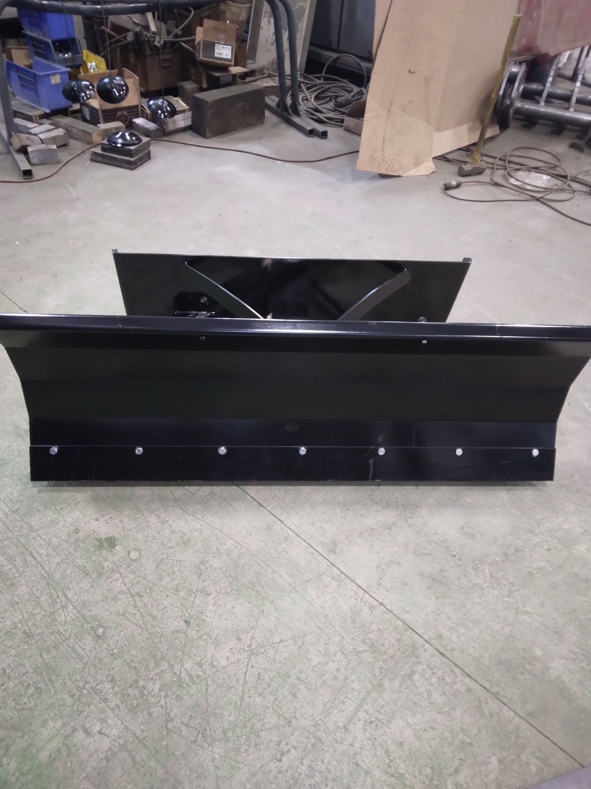 A black snow plow is sitting on a concrete floor