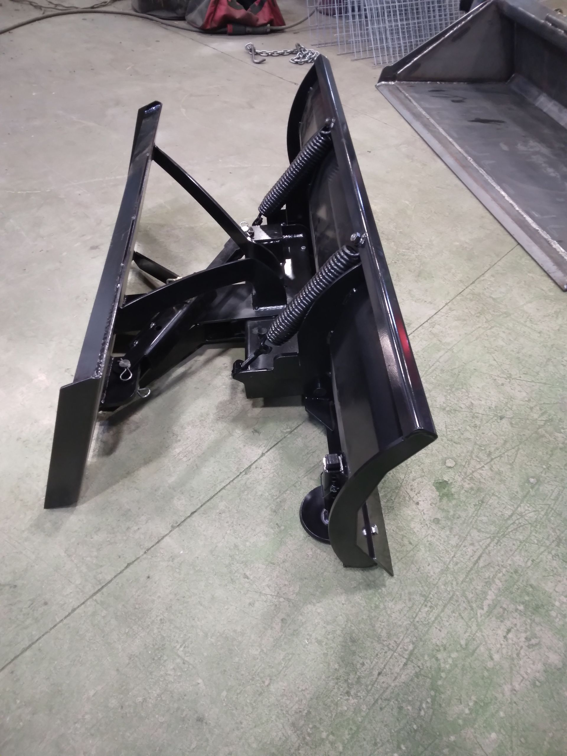 A snow plow is sitting on the floor next to a bucket.