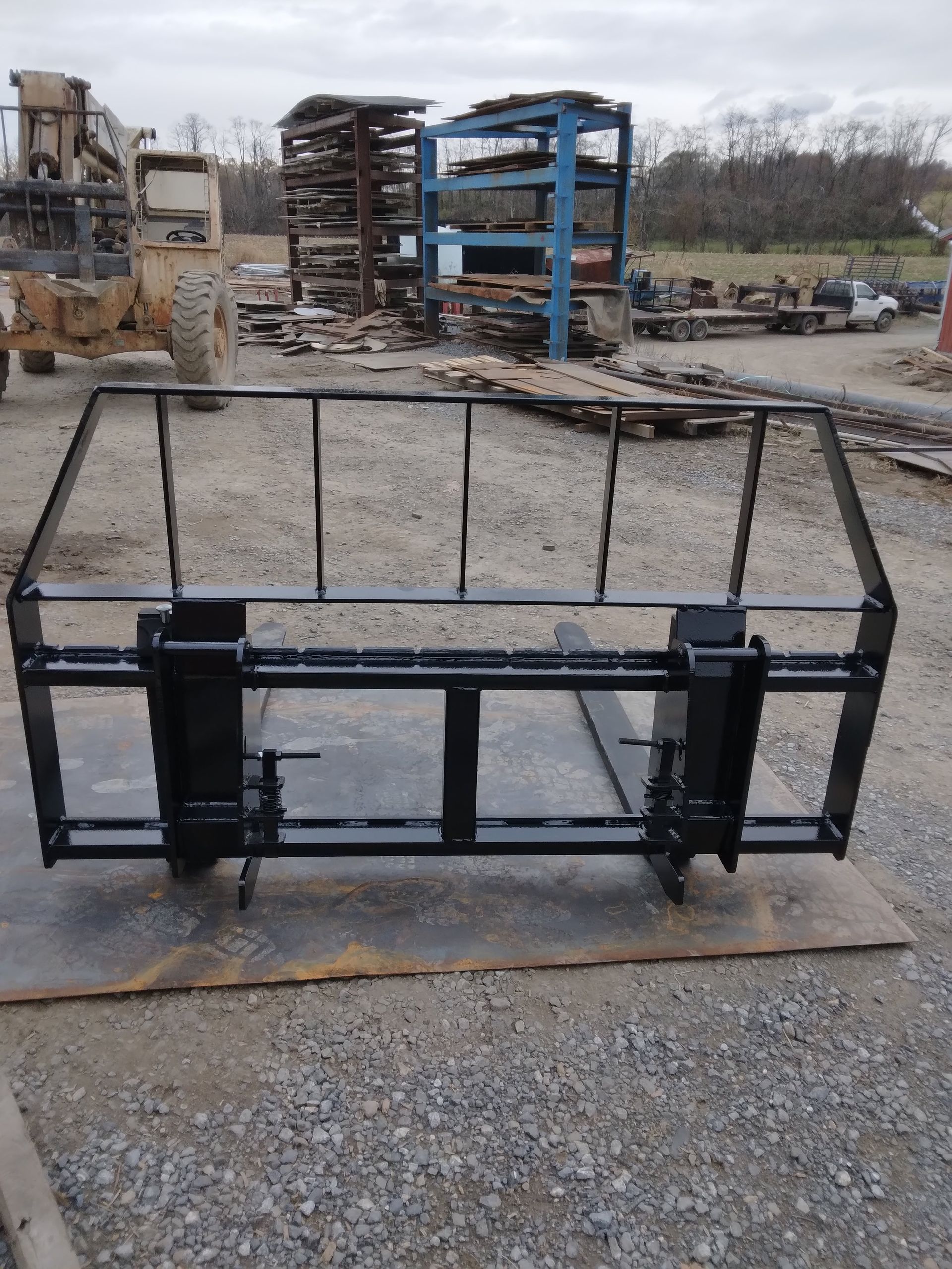 A forklift attachment is sitting on the ground in a gravel area