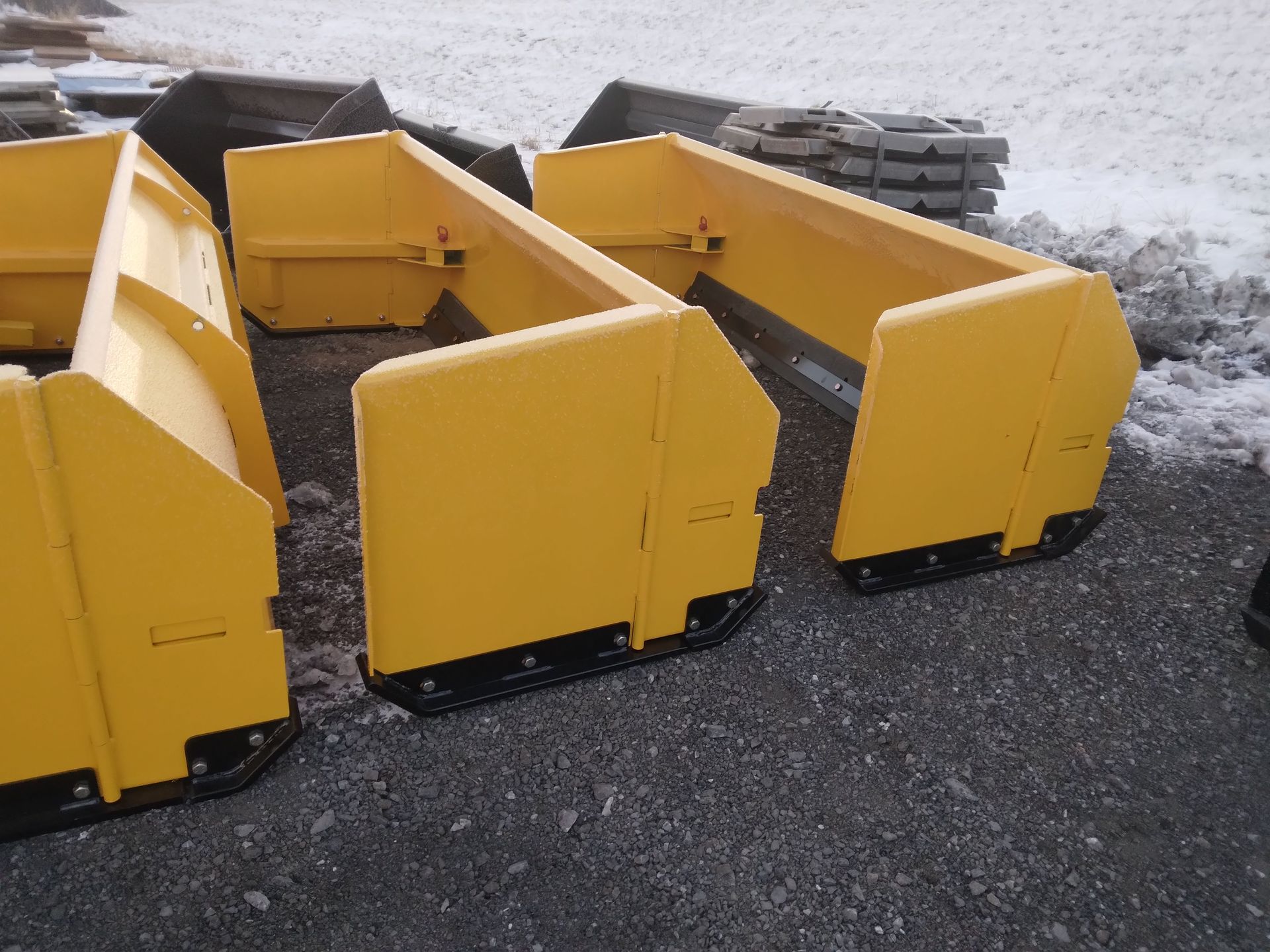 A row of yellow snow plows are sitting on the ground