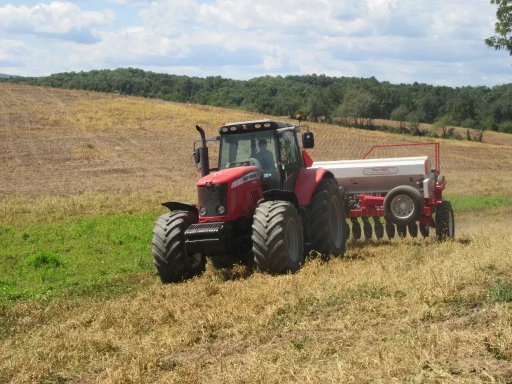 A red tractor is plowing a field with a spreader attached to it