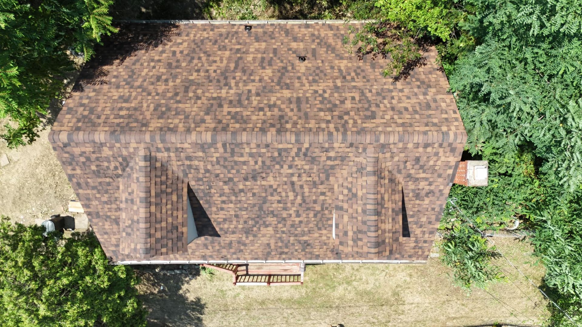 An aerial view of a house with a brown roof surrounded by trees.