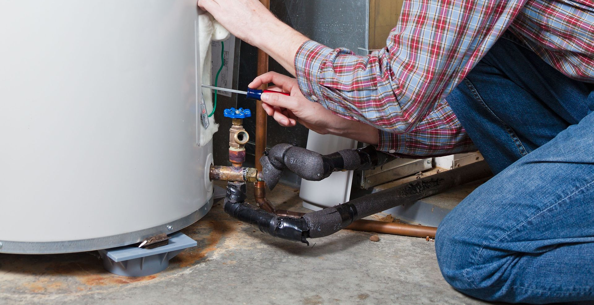 Man in safety glasses working on a water heater in a utility room.