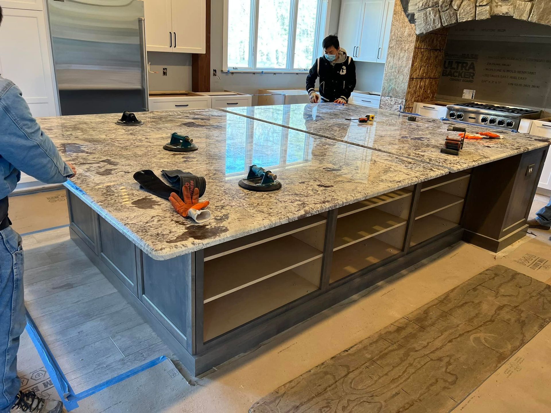 A man is standing next to a large granite counter top in a kitchen.