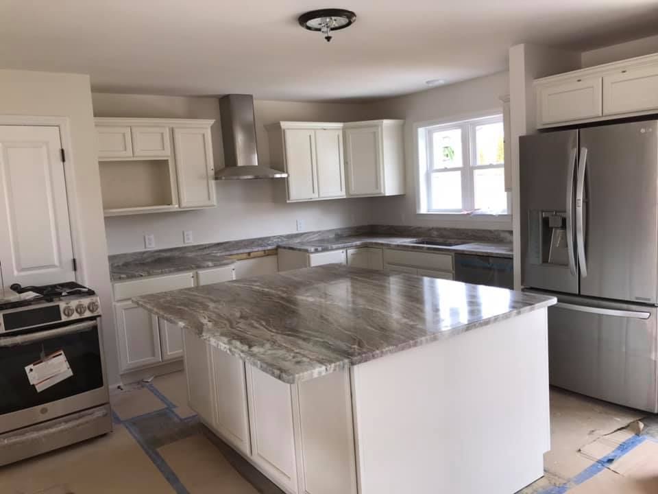 A kitchen with white cabinets , granite counter tops , stainless steel appliances and a large island.