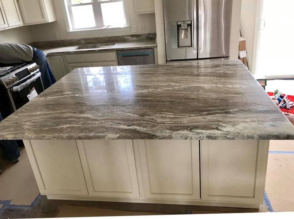 A kitchen with a large granite counter top and white cabinets.