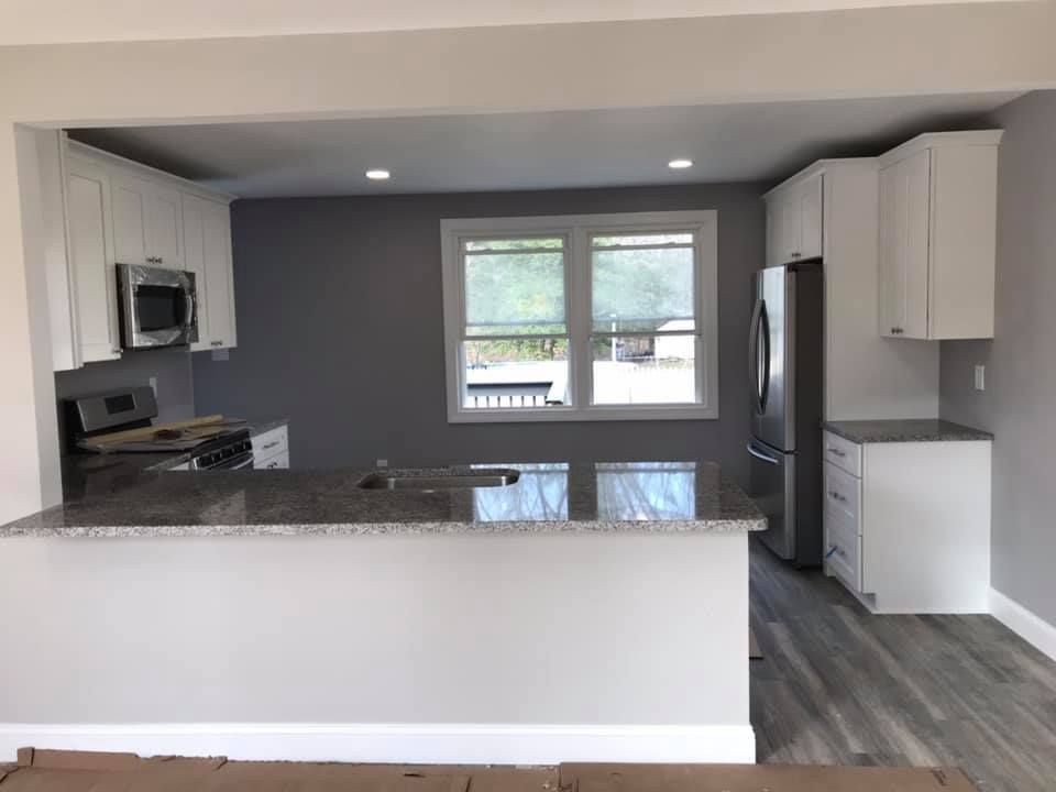 A kitchen with white cabinets , granite counter tops , stainless steel appliances and a refrigerator.
