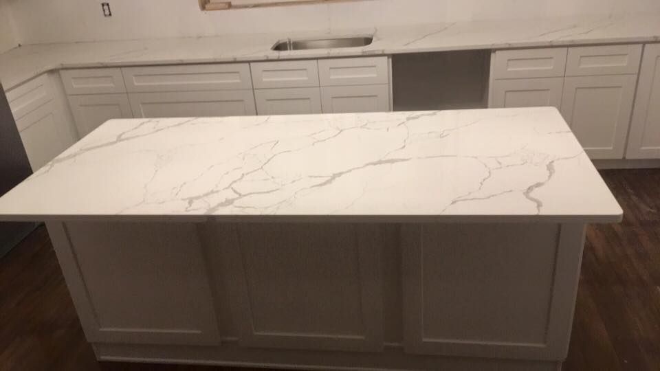 A kitchen with white cabinets and a large island with a marble counter top.