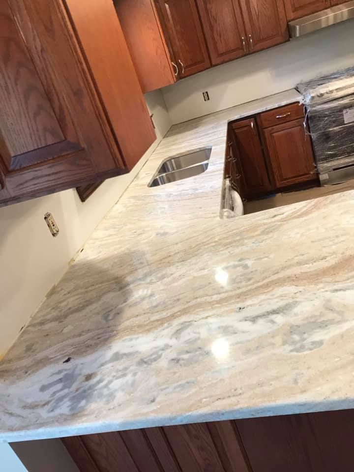 A kitchen with a granite counter top , sink , stove and cabinets.